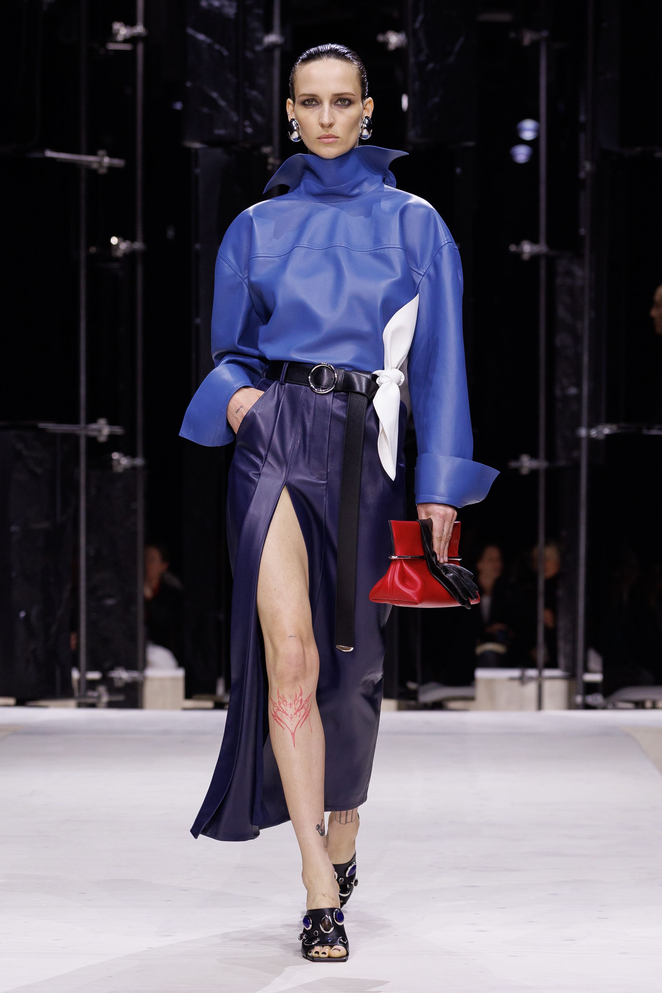 Givenchy 2026秋冬在现代建筑空间中呈现一场充满戏剧性的时装叙事：雕塑式西装、亮色斗篷、结构礼服与夸张装饰共同构建品牌标志性的高级时装气质。蓝色、红色与黄色的高饱和色彩与黑白经典形成鲜明对比，服装通过立体剪裁与夸张廓形展现出强烈视觉张力。整场系列在优雅与戏剧之间取得平衡，展现现代高级时装的力量-顽石频道趋势研究